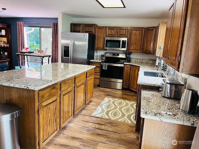 kitchen featuring stainless steel appliances, light stone countertops, light hardwood / wood-style flooring, and a center island