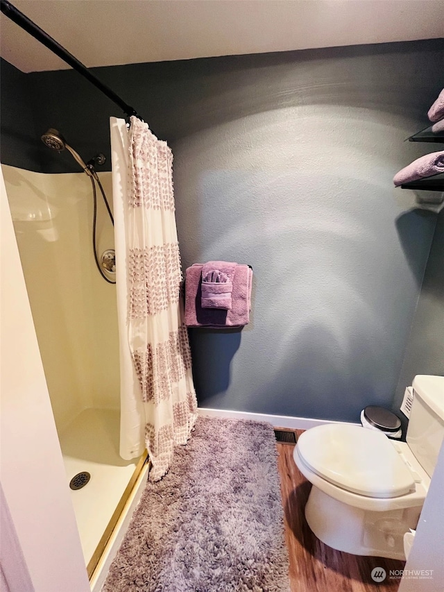 bathroom with wood-type flooring, toilet, and a shower with curtain