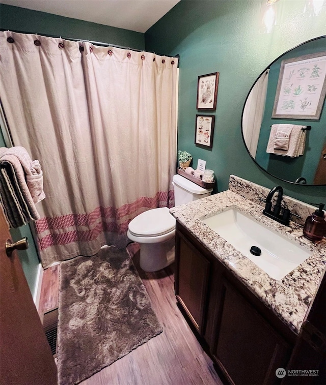 bathroom with wood-type flooring, vanity, walk in shower, and toilet