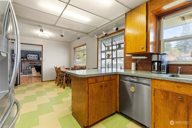 kitchen with a paneled ceiling, sink, kitchen peninsula, backsplash, and appliances with stainless steel finishes