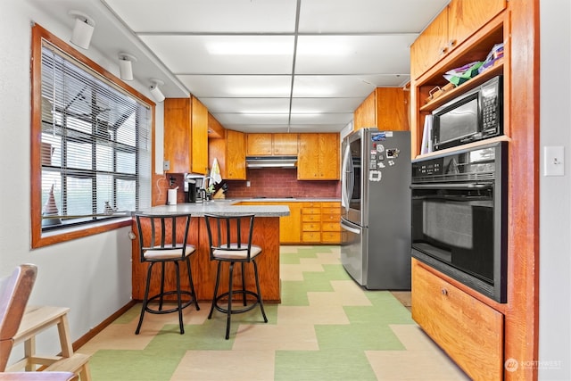 kitchen featuring sink, kitchen peninsula, tasteful backsplash, black appliances, and a breakfast bar area