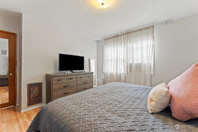 bedroom featuring a textured ceiling, light wood-type flooring, and heating unit