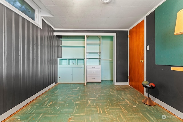 interior space featuring ornamental molding, a closet, wooden walls, and dark parquet floors