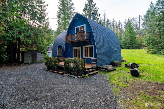 a-frame style home featuring a front yard, a gambrel roof, a balcony, an outbuilding, and a storage unit