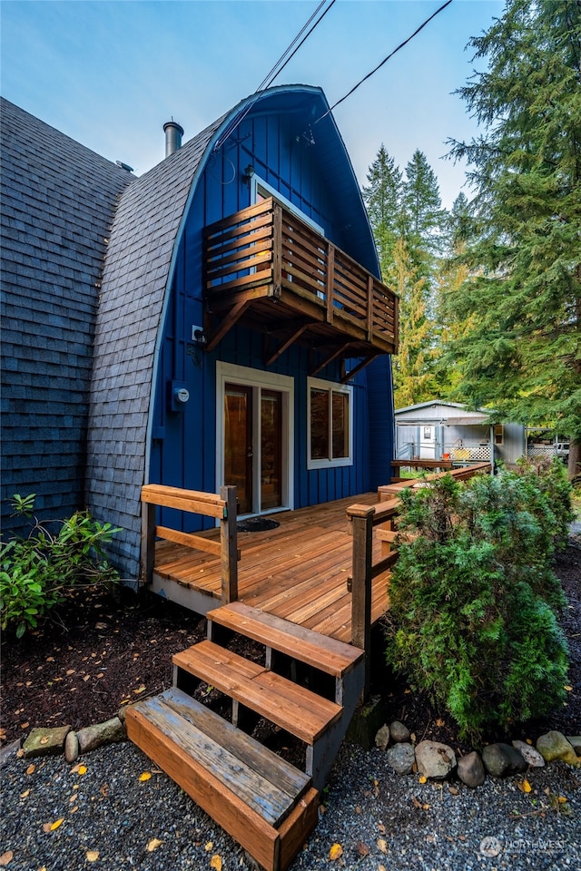 rear view of property featuring roof with shingles, a wooden deck, board and batten siding, and a balcony