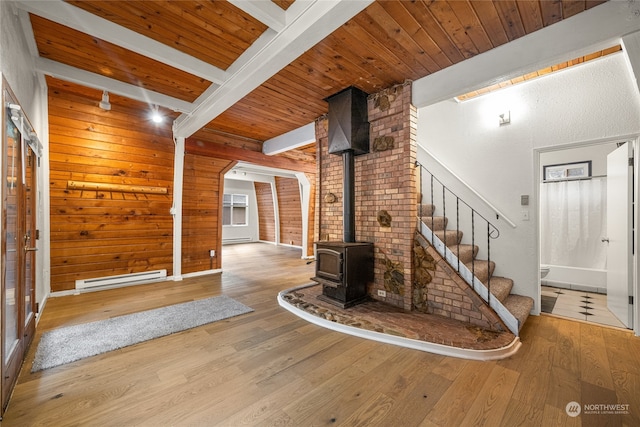 unfurnished living room with light wood-type flooring, wooden ceiling, beam ceiling, a baseboard radiator, and a wood stove