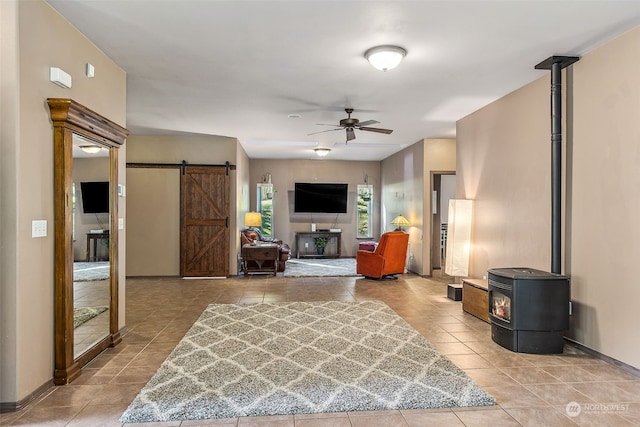 tiled living room with ceiling fan, a barn door, and a wood stove