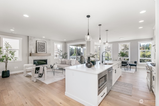 kitchen featuring sink, white cabinetry, an island with sink, pendant lighting, and a high end fireplace