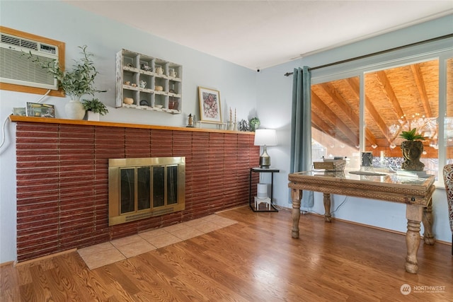 living room featuring lofted ceiling, hardwood / wood-style floors, a fireplace, and a wall unit AC