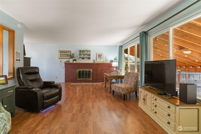 living room with a brick fireplace, an AC wall unit, and light hardwood / wood-style flooring