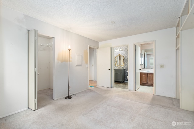 unfurnished bedroom with light carpet, a closet, a textured ceiling, and ensuite bath