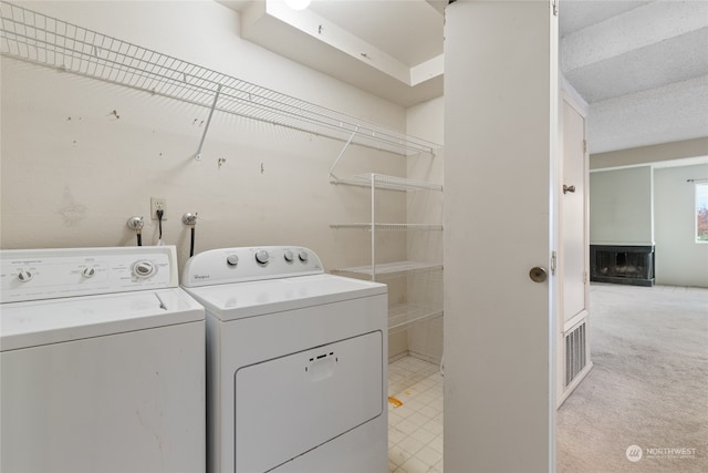 laundry room with a textured ceiling, independent washer and dryer, and light colored carpet