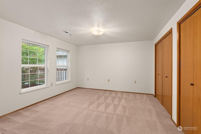 unfurnished bedroom featuring light carpet, a textured ceiling, and multiple closets