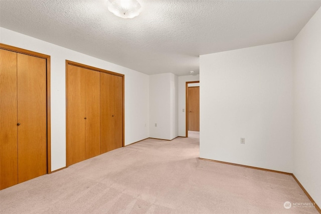 unfurnished bedroom featuring a textured ceiling, light carpet, and two closets