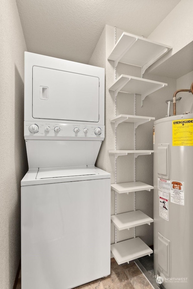 laundry area with dark tile patterned flooring, stacked washer / drying machine, and water heater