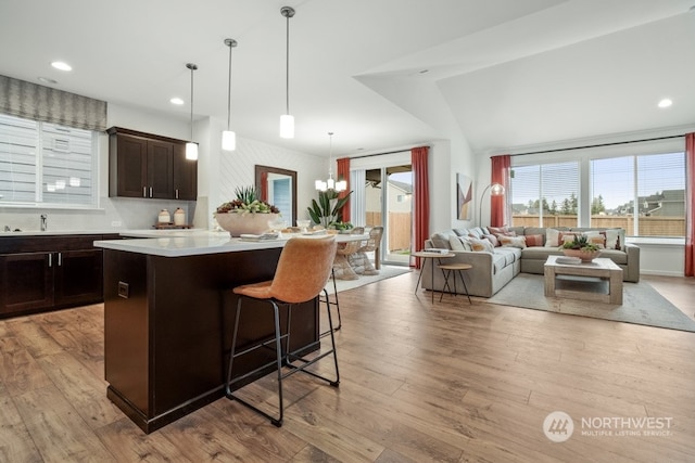 kitchen with light hardwood / wood-style flooring, a kitchen breakfast bar, decorative light fixtures, lofted ceiling, and a center island