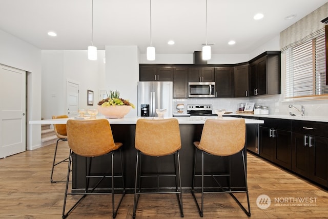 kitchen with pendant lighting, light hardwood / wood-style floors, appliances with stainless steel finishes, and a kitchen island