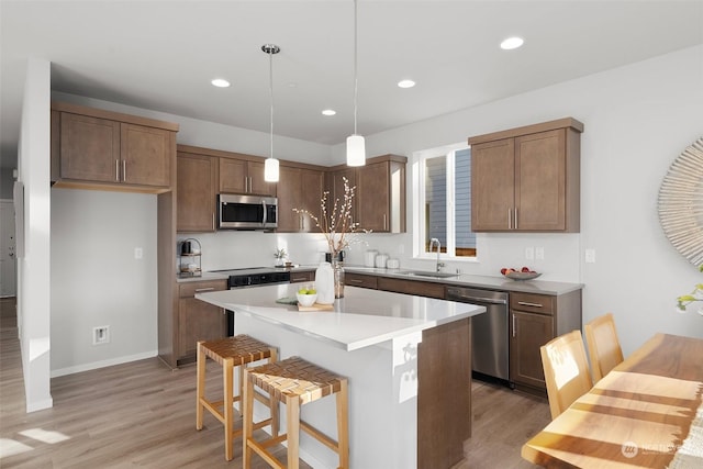 kitchen with sink, hanging light fixtures, light hardwood / wood-style flooring, appliances with stainless steel finishes, and a kitchen island