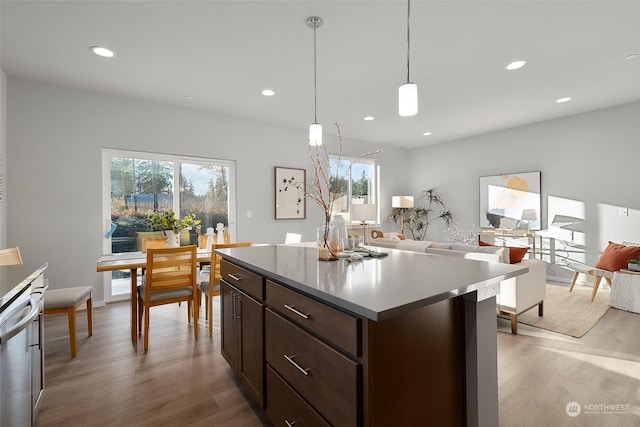 kitchen featuring pendant lighting, dark brown cabinetry, light hardwood / wood-style floors, a kitchen island, and stainless steel dishwasher