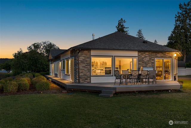 back house at dusk featuring a wooden deck and a lawn