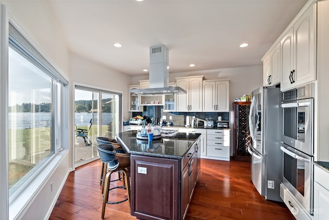 kitchen featuring a kitchen island, dark hardwood / wood-style floors, stainless steel appliances, island range hood, and a kitchen breakfast bar