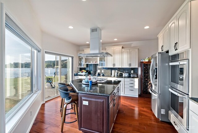 1558 Fairview St, Bellingham, WA 98229 - kitchen featuring appliances with stainless steel finishes, island range hood, a breakfast bar, decorative backsplash, and dark wood-style floors