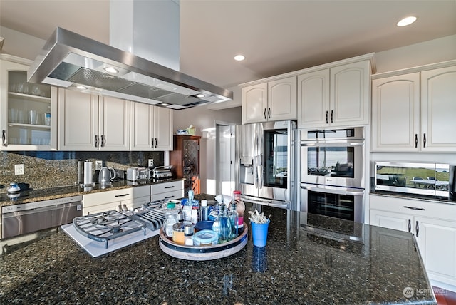 kitchen with tasteful backsplash, dark stone countertops, stainless steel appliances, white cabinets, and island range hood