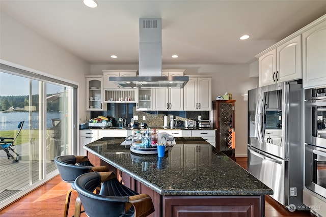 kitchen featuring island exhaust hood, appliances with stainless steel finishes, hardwood / wood-style flooring, and white cabinetry