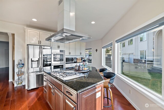 1558 Fairview St, Bellingham, WA 98229 - kitchen with stainless steel appliances, island range hood, dark wood-style flooring, dark stone counters, and a kitchen bar