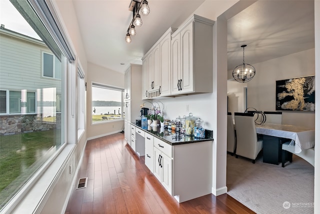 kitchen featuring white cabinets, dark wood-type flooring, pendant lighting, dark stone counters, and a notable chandelier