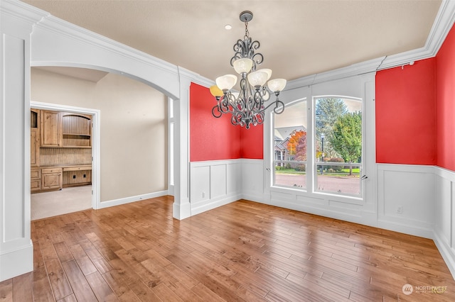 unfurnished dining area featuring a notable chandelier, ornamental molding, and wood-type flooring