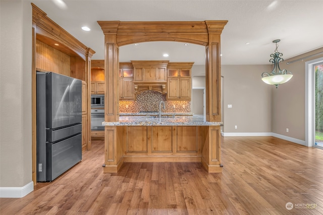 kitchen with appliances with stainless steel finishes, light stone counters, light wood-type flooring, and pendant lighting