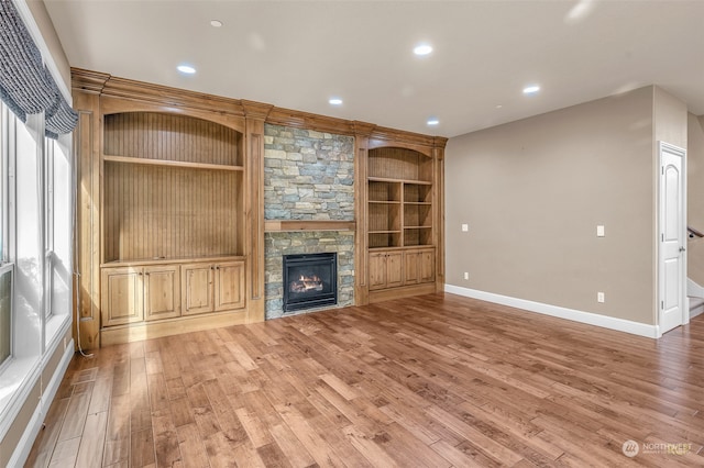 unfurnished living room with a stone fireplace, hardwood / wood-style flooring, and built in features