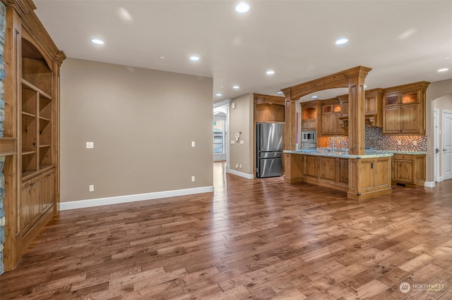 kitchen with hardwood / wood-style floors, tasteful backsplash, appliances with stainless steel finishes, sink, and light stone counters