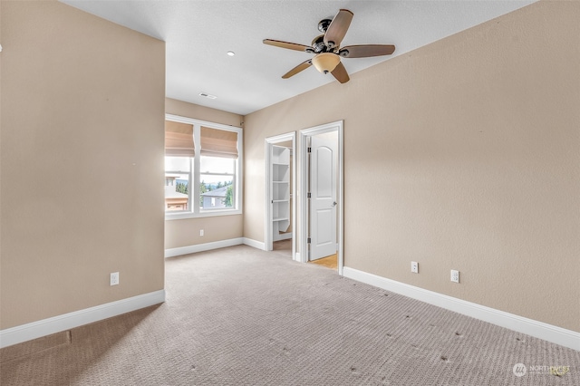 unfurnished bedroom featuring light carpet, a walk in closet, and ceiling fan