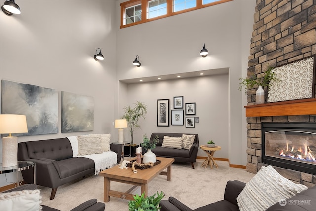 carpeted living room featuring a stone fireplace and a high ceiling