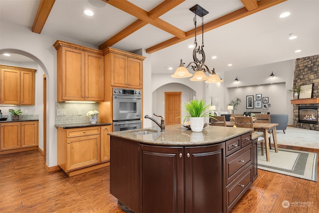 kitchen with wood-type flooring, a center island with sink, a fireplace, and hanging light fixtures