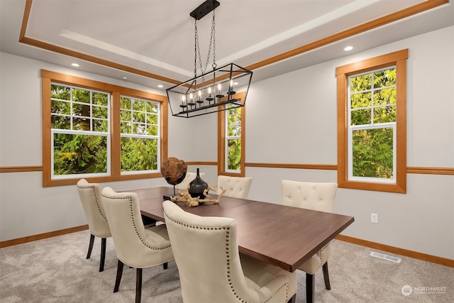 dining area with light colored carpet, a notable chandelier, and a tray ceiling