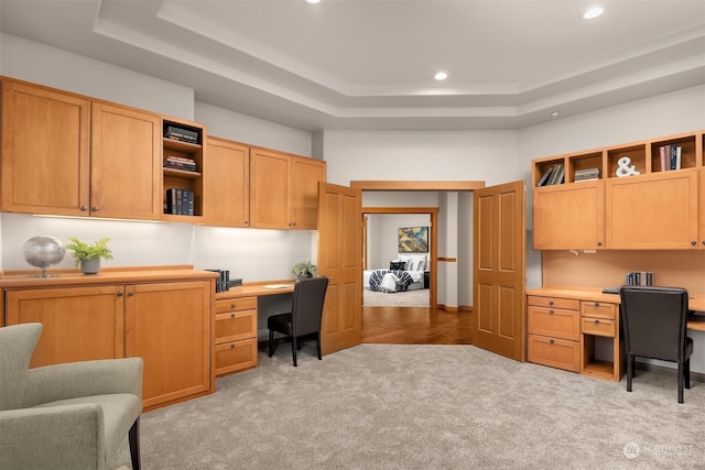 carpeted office with a raised ceiling and built in desk