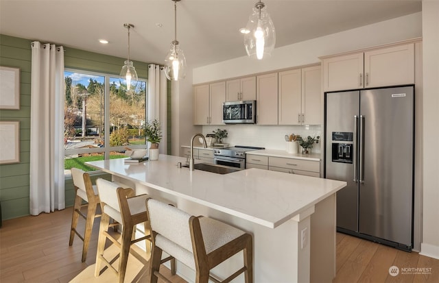 kitchen with sink, appliances with stainless steel finishes, hanging light fixtures, a center island with sink, and light wood-type flooring