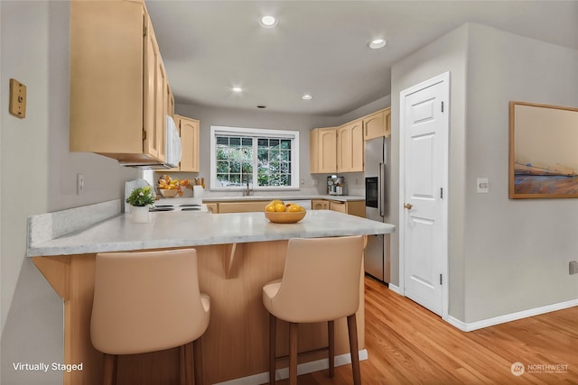 kitchen with light wood-type flooring, kitchen peninsula, stainless steel fridge, a kitchen breakfast bar, and light brown cabinets