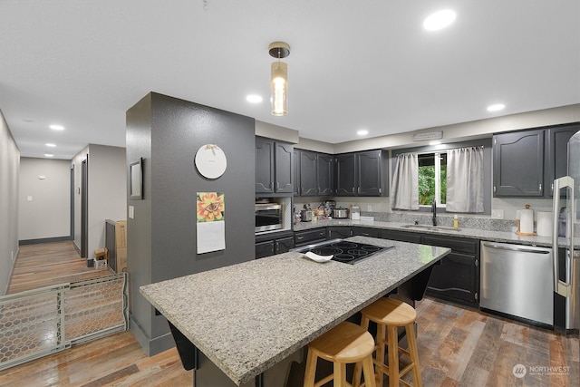 kitchen with wood-type flooring, stainless steel appliances, light stone counters, and sink