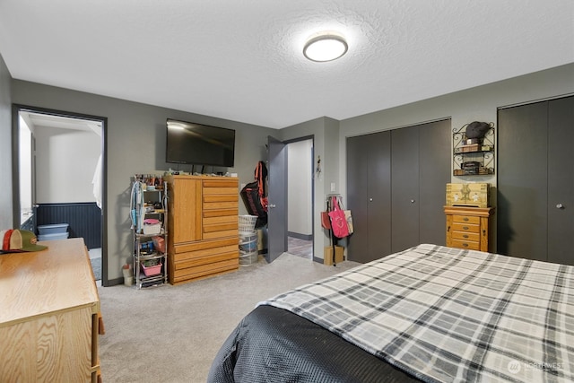 bedroom featuring a textured ceiling, multiple closets, and light colored carpet