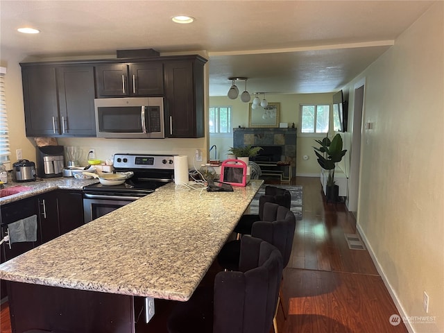 kitchen featuring light stone counters, stainless steel appliances, dark wood-type flooring, a tiled fireplace, and a breakfast bar area