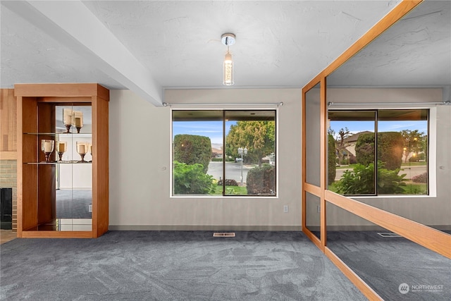 unfurnished room with a fireplace, carpet flooring, a textured ceiling, and a healthy amount of sunlight