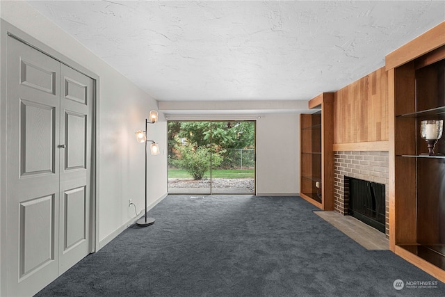 unfurnished living room with dark carpet, a textured ceiling, and a brick fireplace