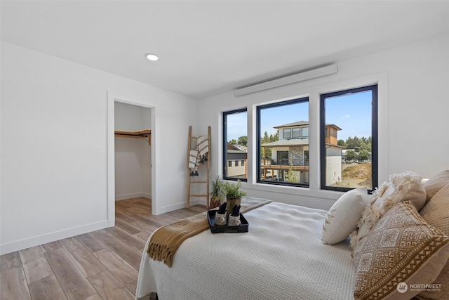 bedroom with a spacious closet, baseboards, light wood-type flooring, and recessed lighting