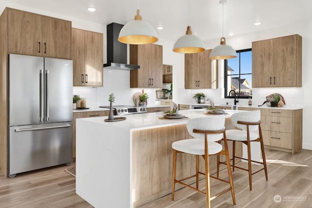 kitchen featuring a kitchen island, wall chimney range hood, hanging light fixtures, light wood-type flooring, and high end fridge