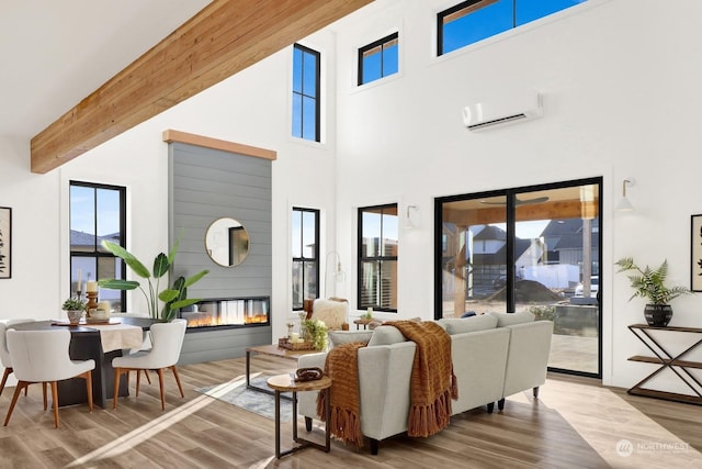 living room with beamed ceiling, hardwood / wood-style flooring, a towering ceiling, and a wall unit AC