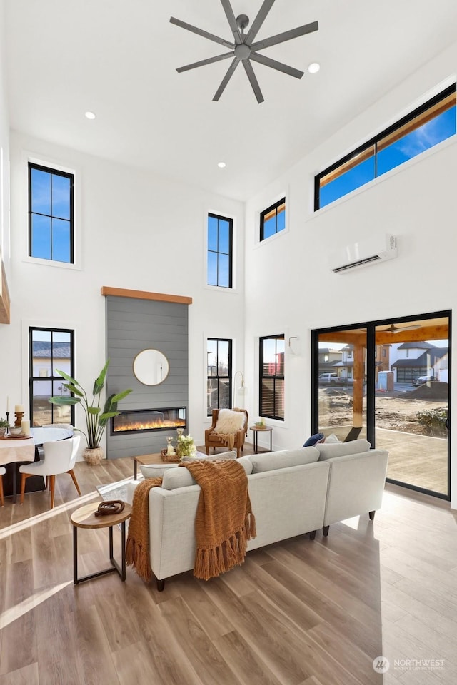 living room with ceiling fan, hardwood / wood-style floors, a wall unit AC, and a towering ceiling